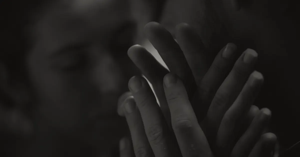 Hands in prayer position, blurred face behind, meditative