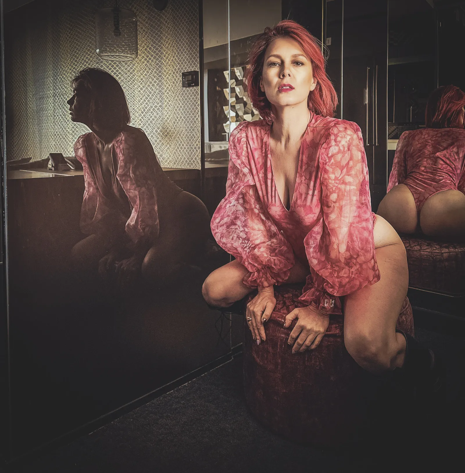 Viktoria in a sheer pink blouse seated on a velvet surface, her reflection in a gold mirror