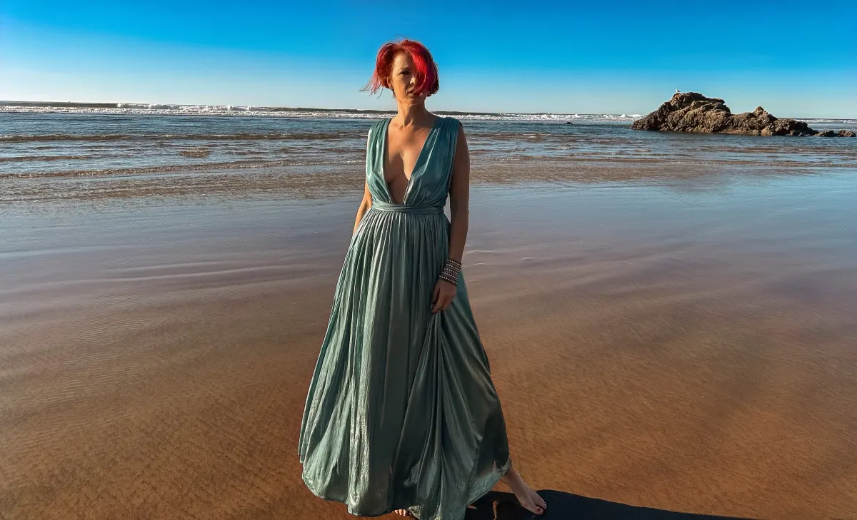 Viktoria in a teal gown standing in shallow ocean water at golden hour