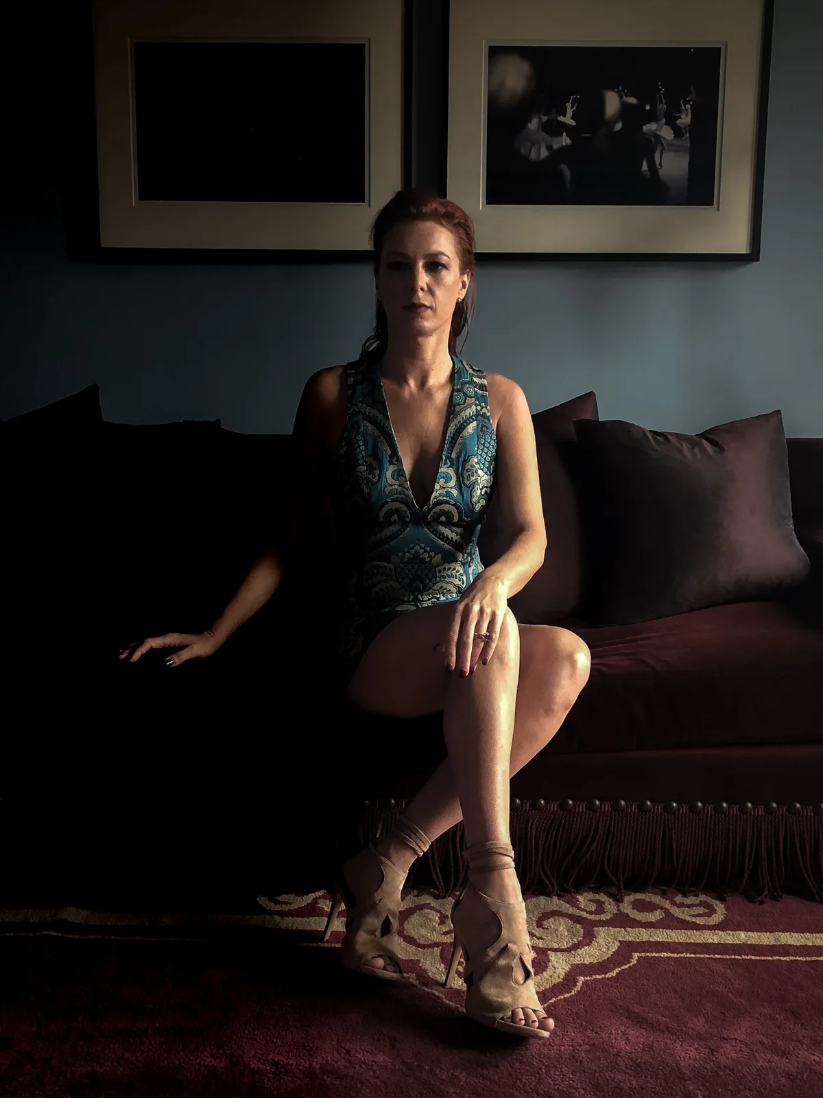 Viktoria Sway seated half in shadow on a dark sofa — BDSM shadow play and conscious kink in NYC