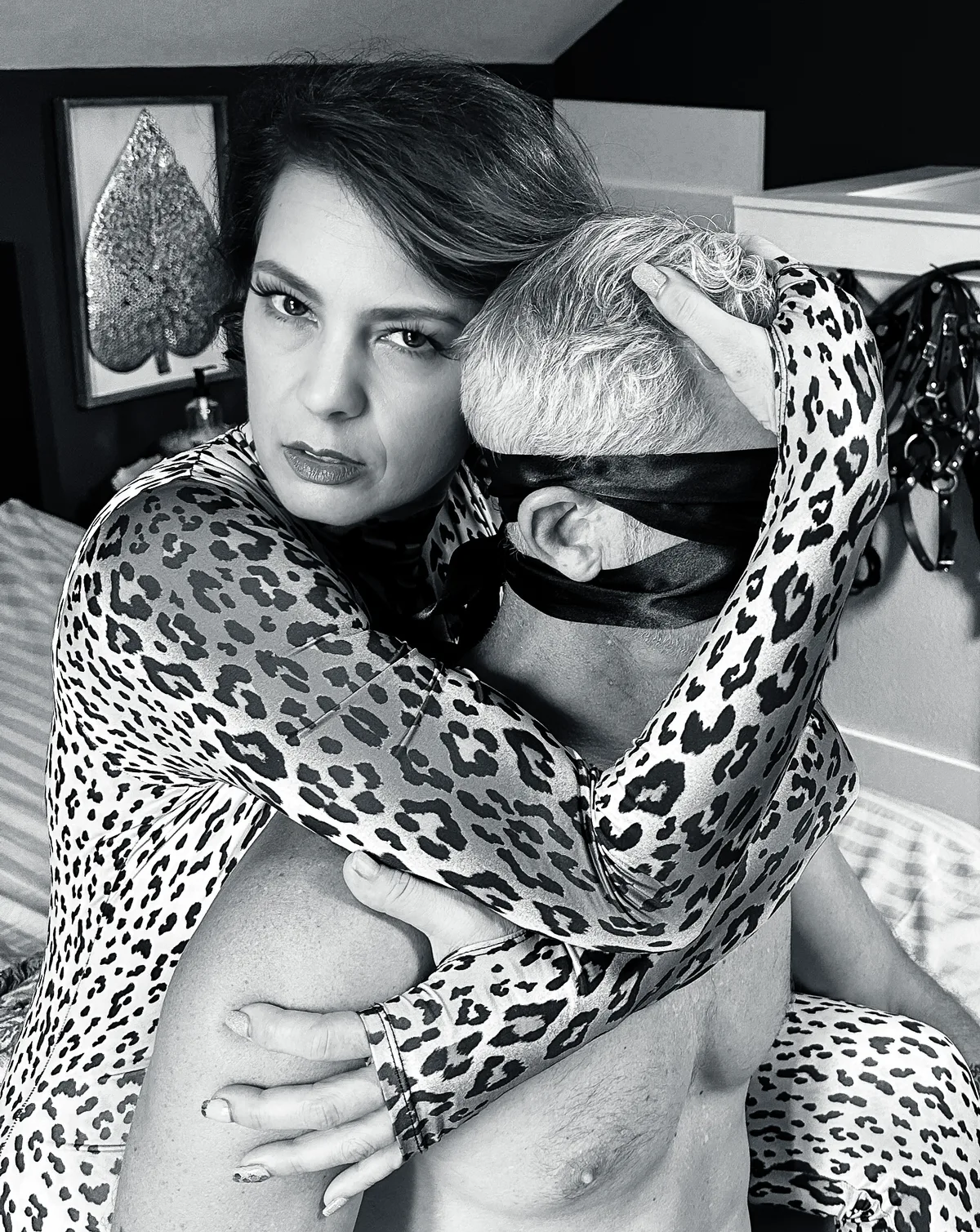 Goddess Viktoria Sway, NYC Dominatrix, in a black and white photo, holding a blindfolded submissive in an intimate, commanding embrace.